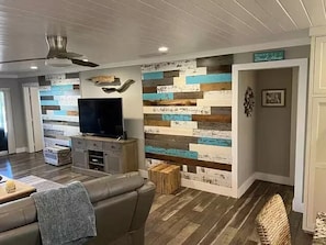 A living room with a flat-screen TV, a sofa, a coffee table, a wooden floor, and a wall with a horizontal wooden plank design. - Aqua Tide Retreat - Waterfront + Boatlift (Jensen Beach)