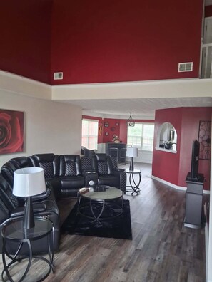 A living room with a black leather sofa, a glass coffee table, and a red accent wall. - Spacious 4-bedroom, 2.5 bath home in beautiful Fairburn with spacious living (Fairburn)