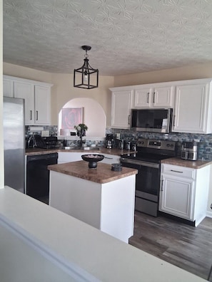 A modern kitchen with white cabinetry, a central island, stainless steel appliances, and a patterned ceiling. - Spacious 4-bedroom, 2.5 bath home in beautiful Fairburn with spacious living (Fairburn)