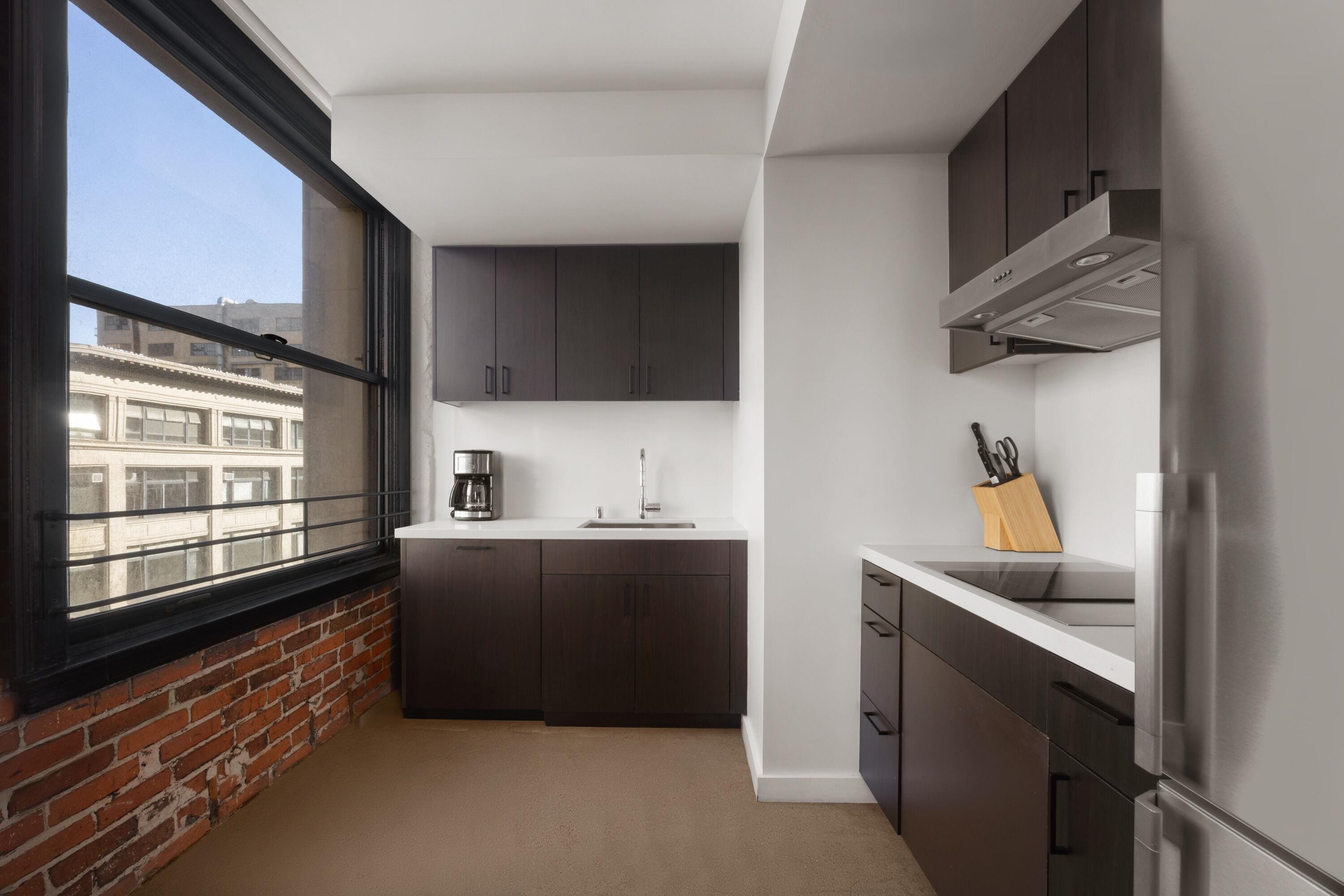 Una cocina compacta con ventana, armarios oscuros, un refrigerador de acero inoxidable y una cafetera.