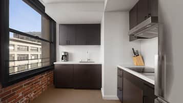 Una cocina compacta con ventana, armarios oscuros, un refrigerador de acero inoxidable y una cafetera.