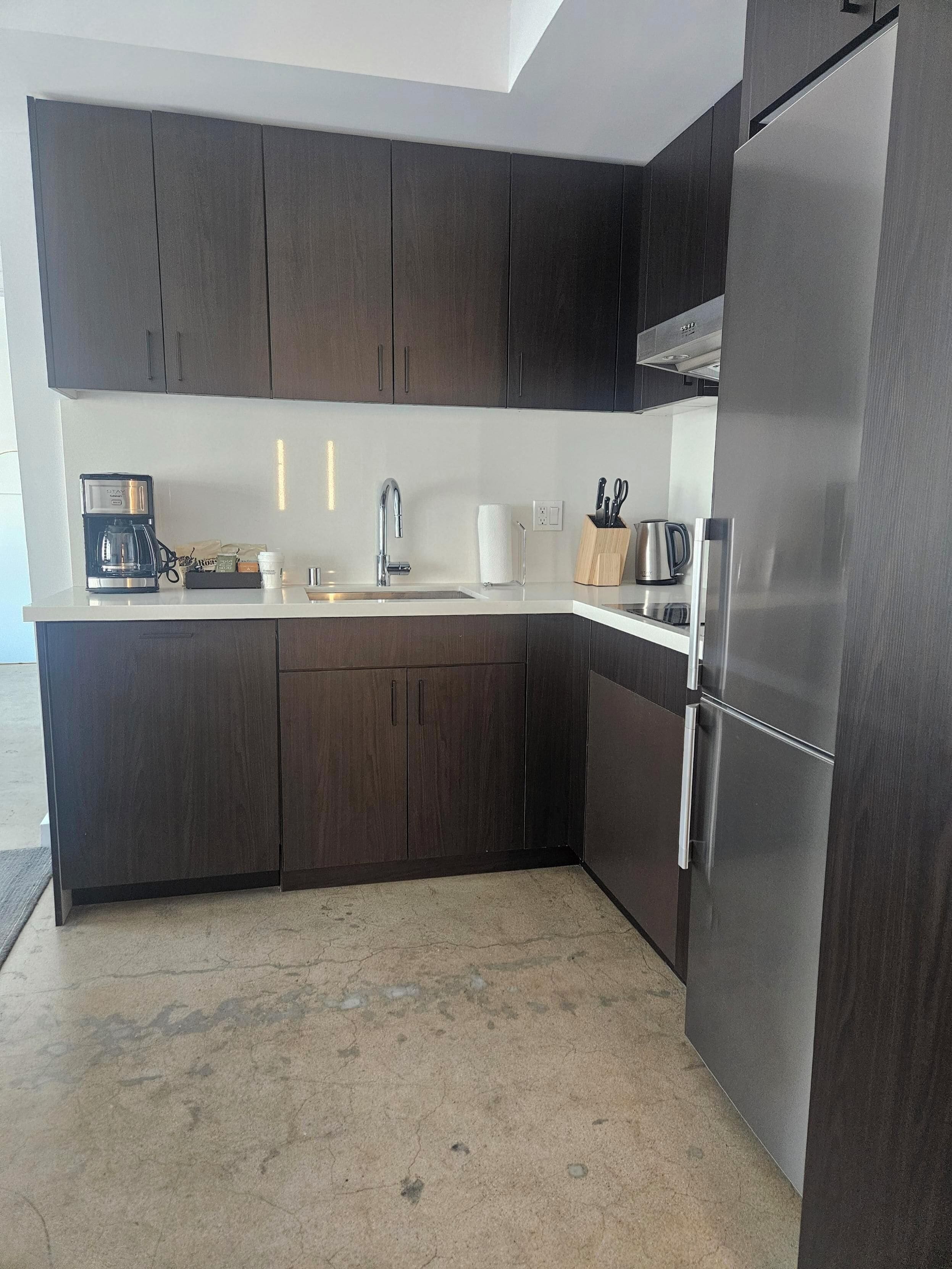Una cucina moderna con mobili in legno scuro, elettrodomestici in acciaio inossidabile e un piano di lavoro bianco.