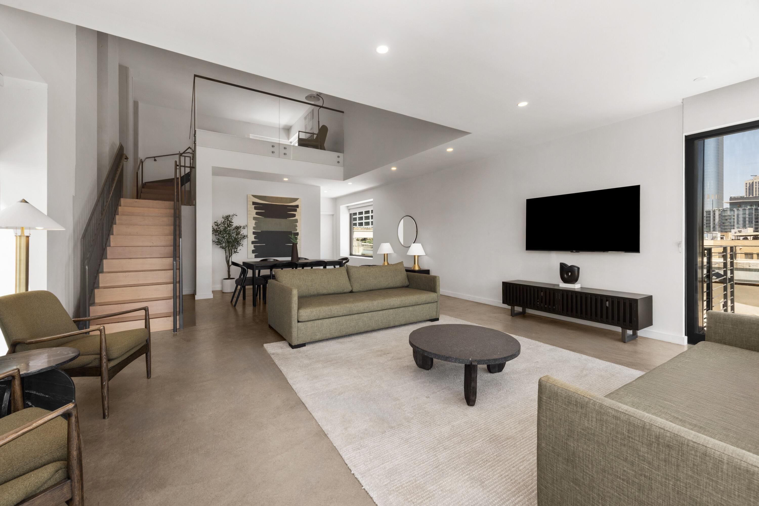 A modern living room with a staircase, a sofa, a coffee table, and a flat-screen TV.