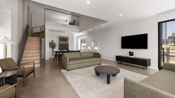 A modern living room with a staircase, a sofa, a coffee table, and a flat-screen TV.