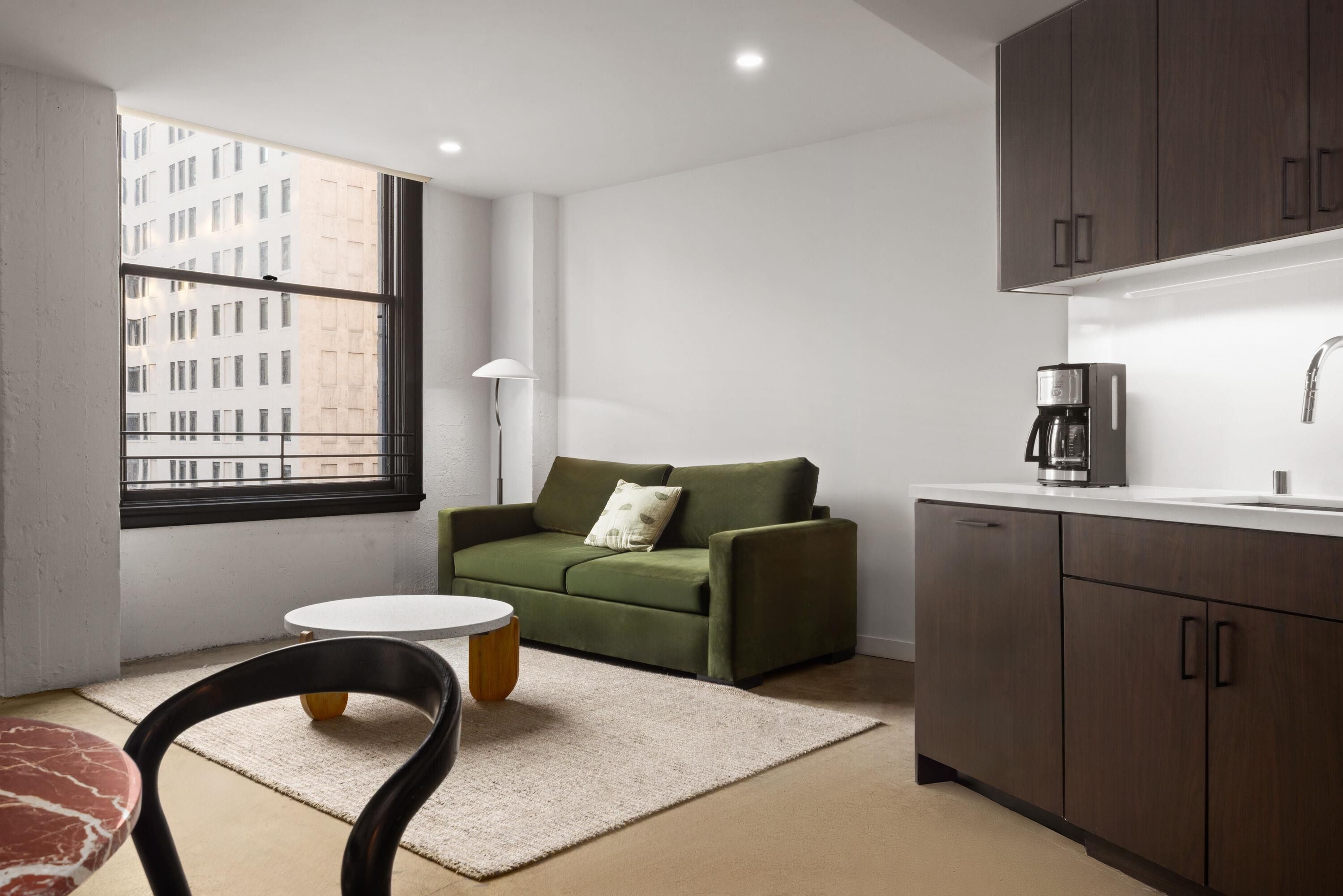 A modern kitchen with a dining area, a sofa, and a window with a view of buildings.