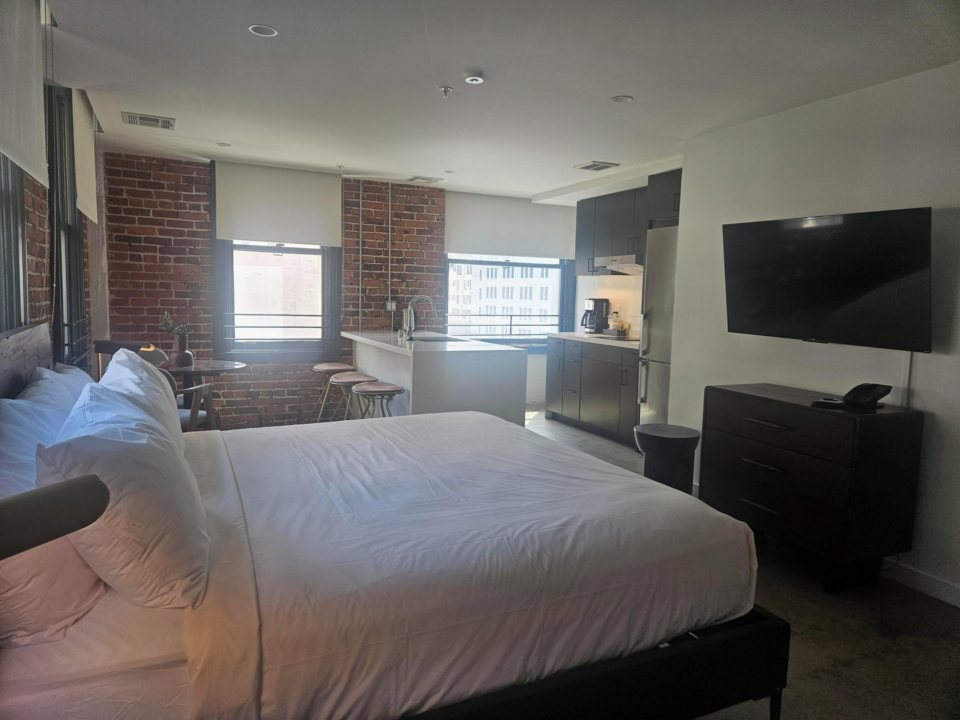Una habitación de hotel moderna con una cama grande, televisión, zona de cocina y vistas a la ciudad.