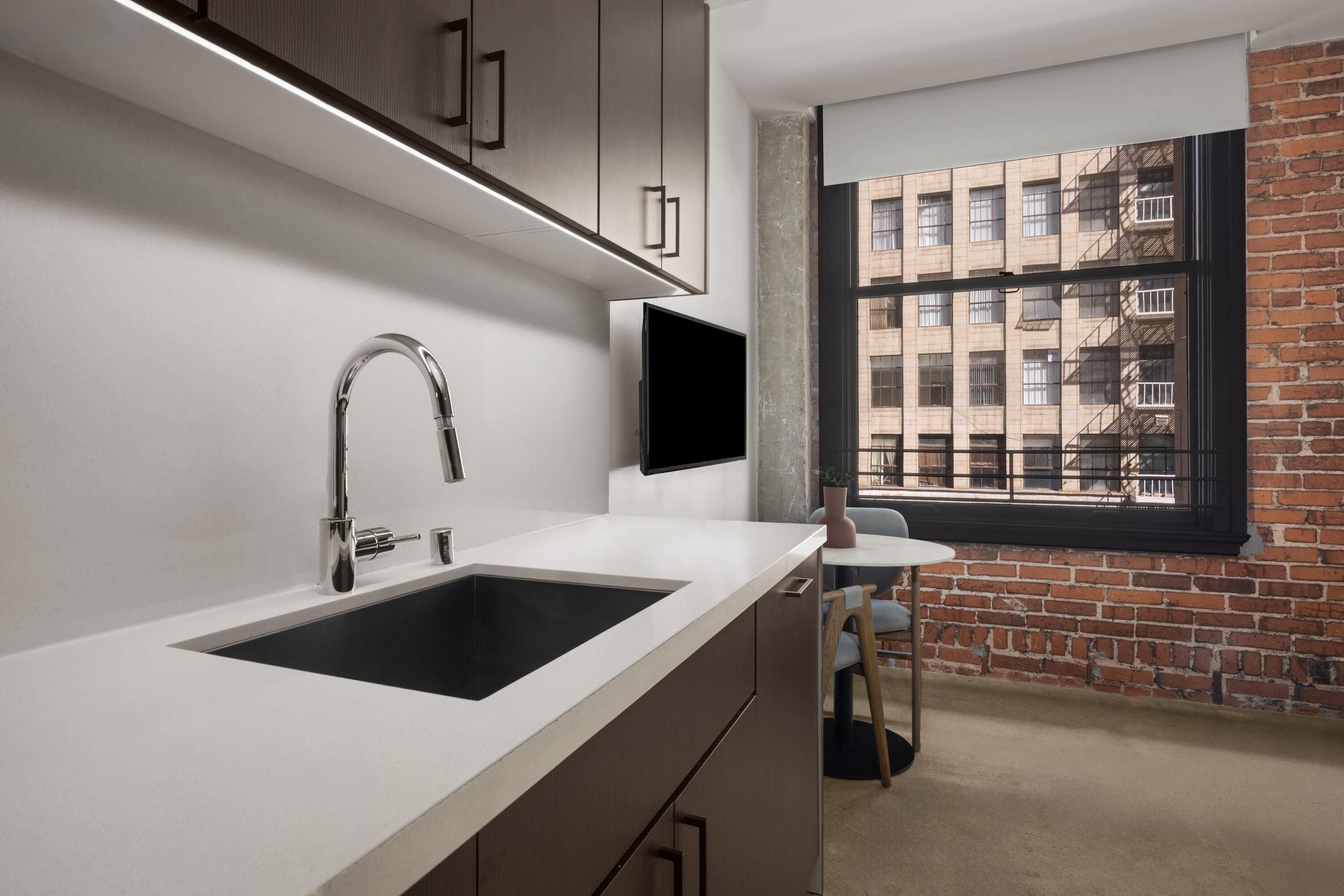 A modern kitchen with a large sink, cabinets, and a window overlooking a brick building.