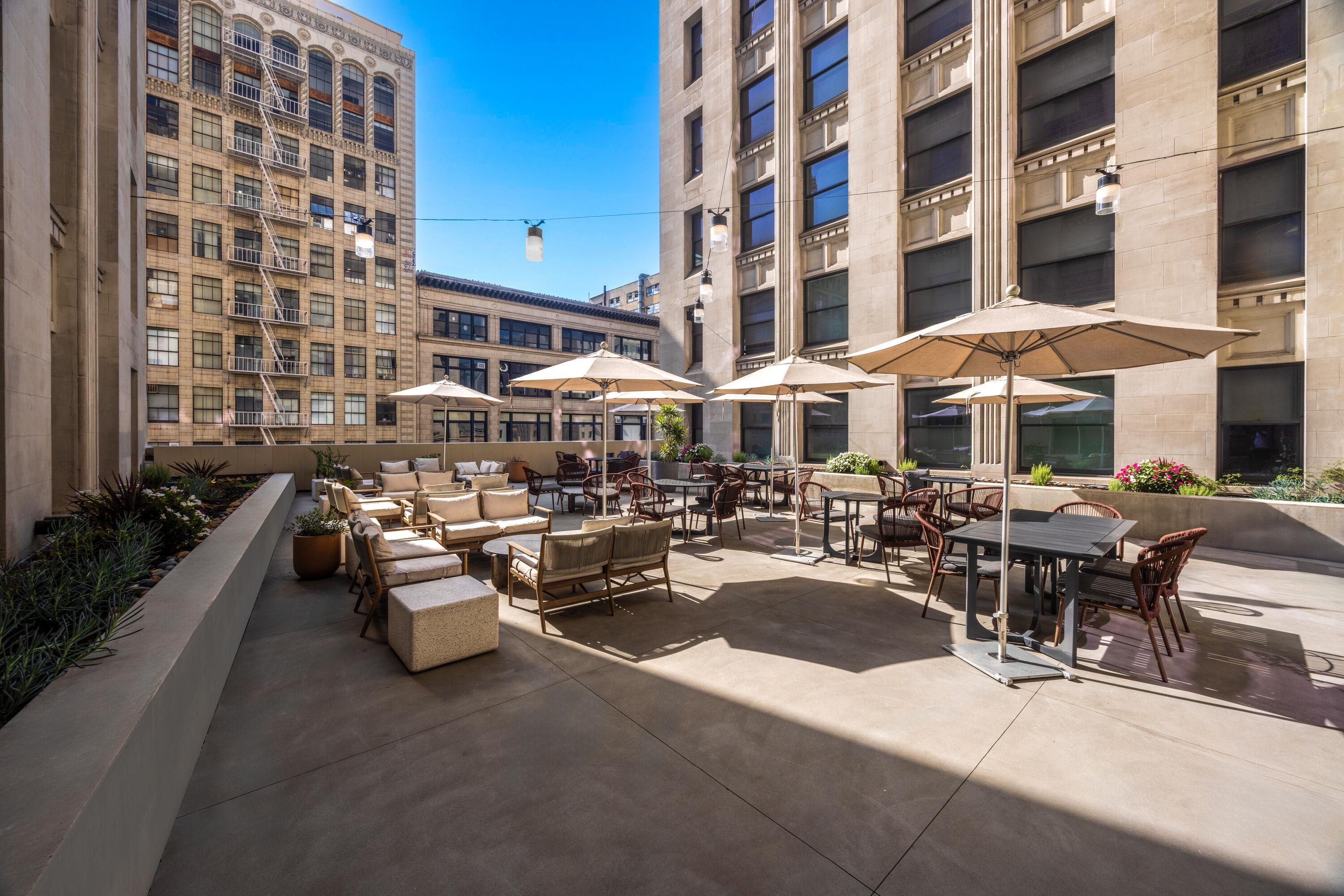 An outdoor patio area with seating arrangements and umbrellas, surrounded by tall buildings.
