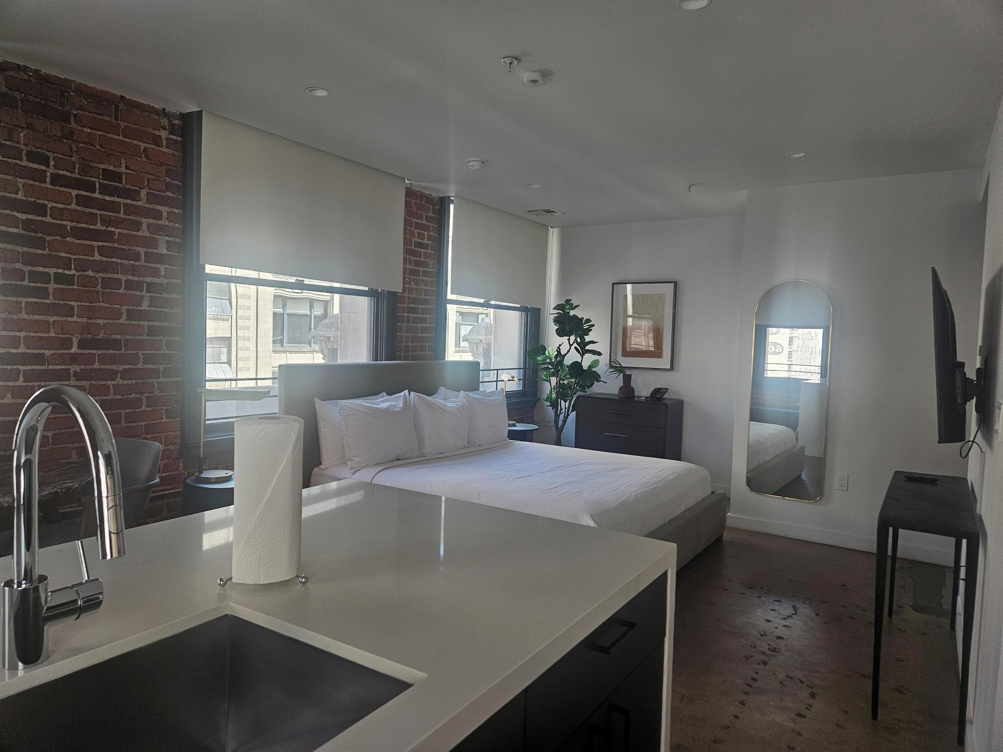 Habitación de hotel moderna con una cama grande, un escritorio pequeño, un espejo y vistas a la ciudad.