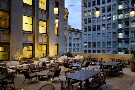 Una terrazza esterna con posti a sedere e tavoli, circondata da edifici con ampie finestre e una scala antincendio.. The Winfield Lofts, A Wyndham Hotel
