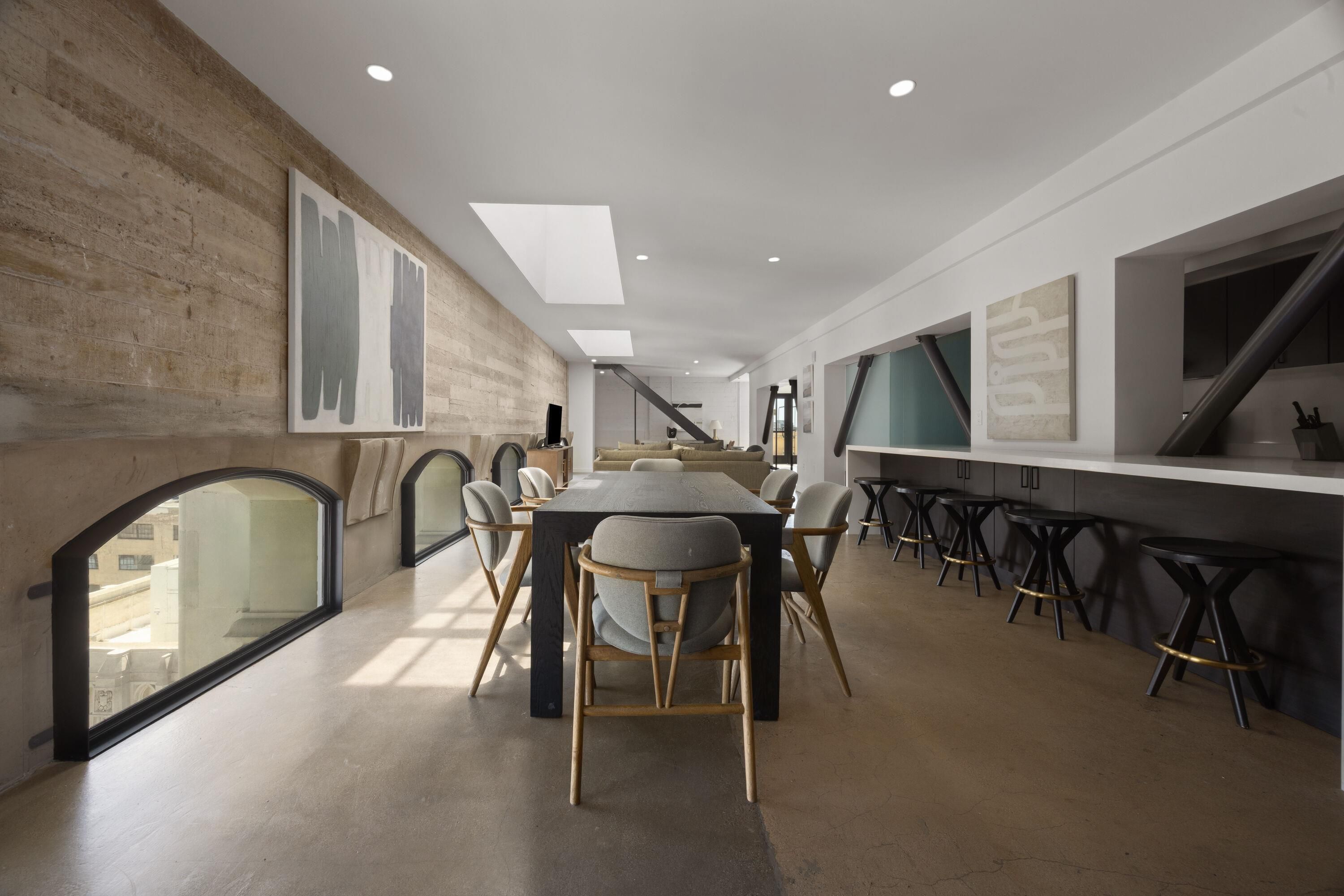 Un espace repas moderne avec une longue table, des chaises et un bar avec des tabourets.