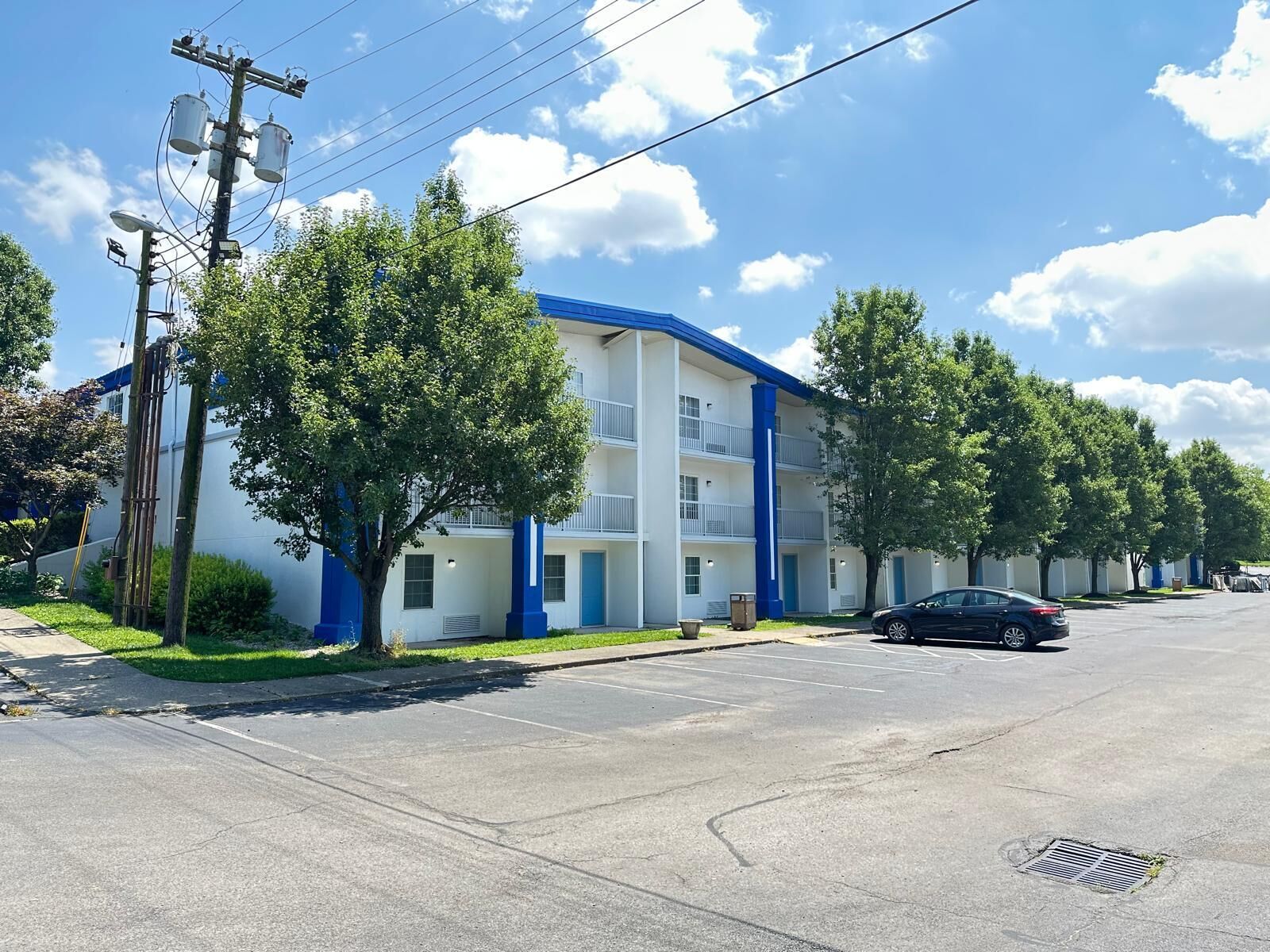 A multi-story building with a blue and white exterior, a parking lot, and a tree-lined street.