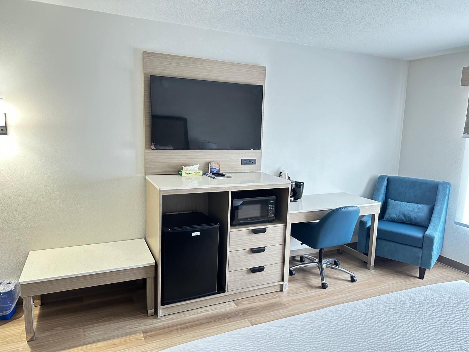Quarto de hotel com escrivaninha, televisão de tela plana, micro-ondas, uma cadeira azul e uma cama.