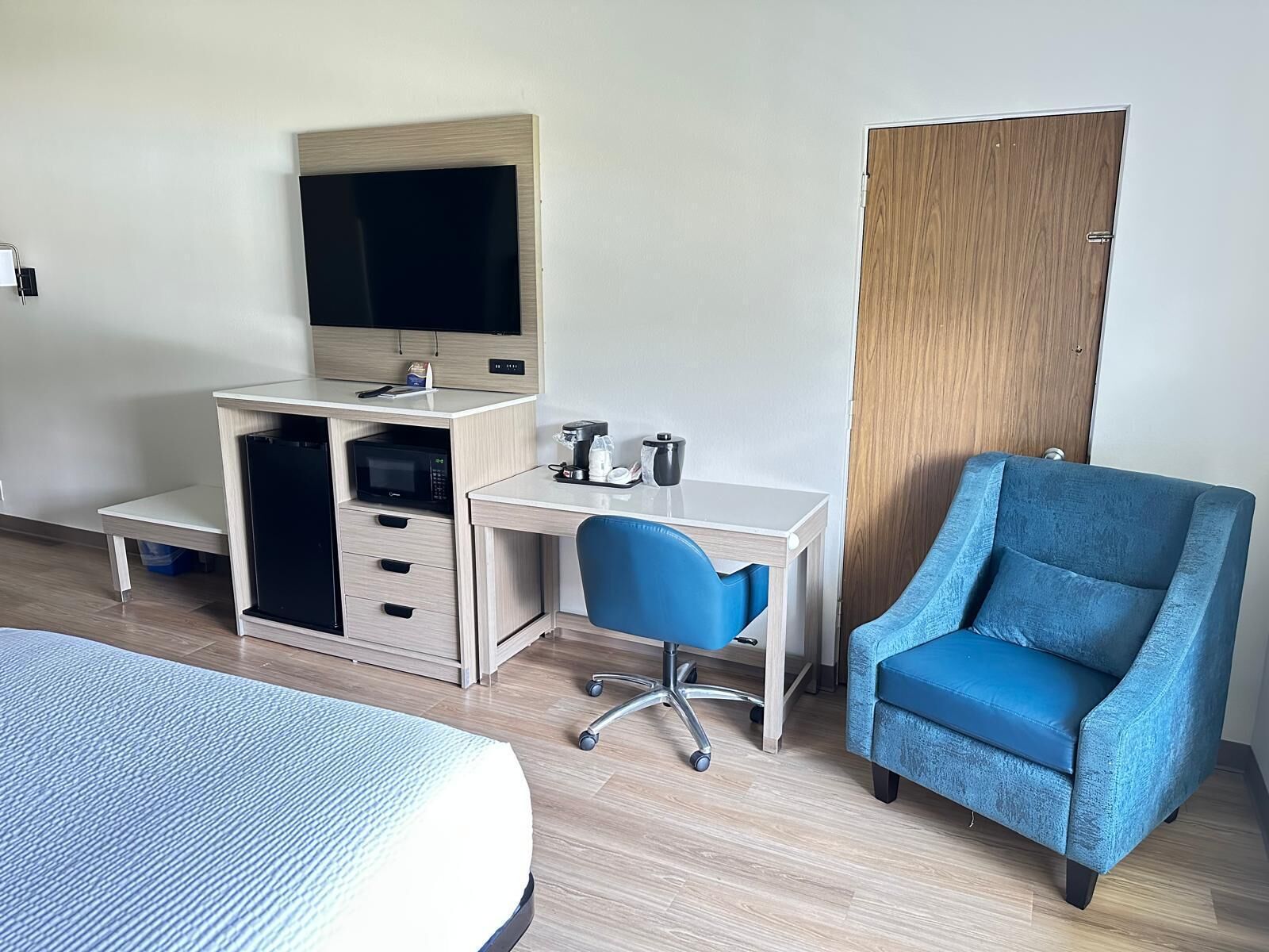 A hotel room with a bed, a desk with a computer, a chair, a wardrobe, and a television.