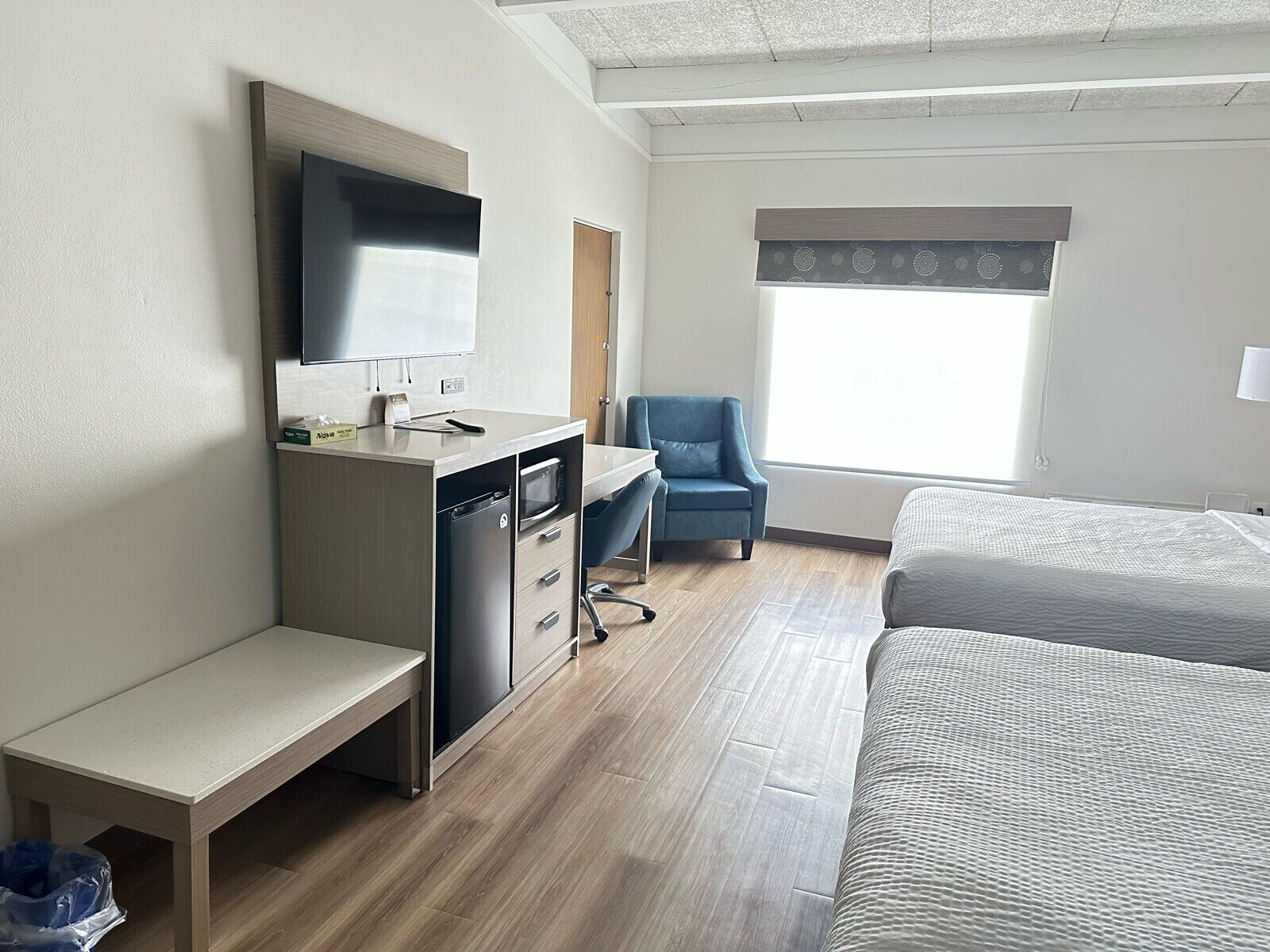 Una camera d'albergo con una scrivania, una sedia, un letto e un'ampia finestra.