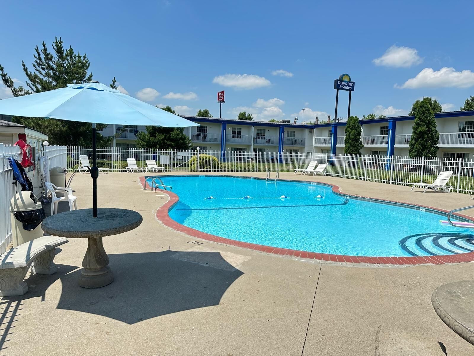 A swimming pool with lounge chairs, a covered area, and a fenced poolside.