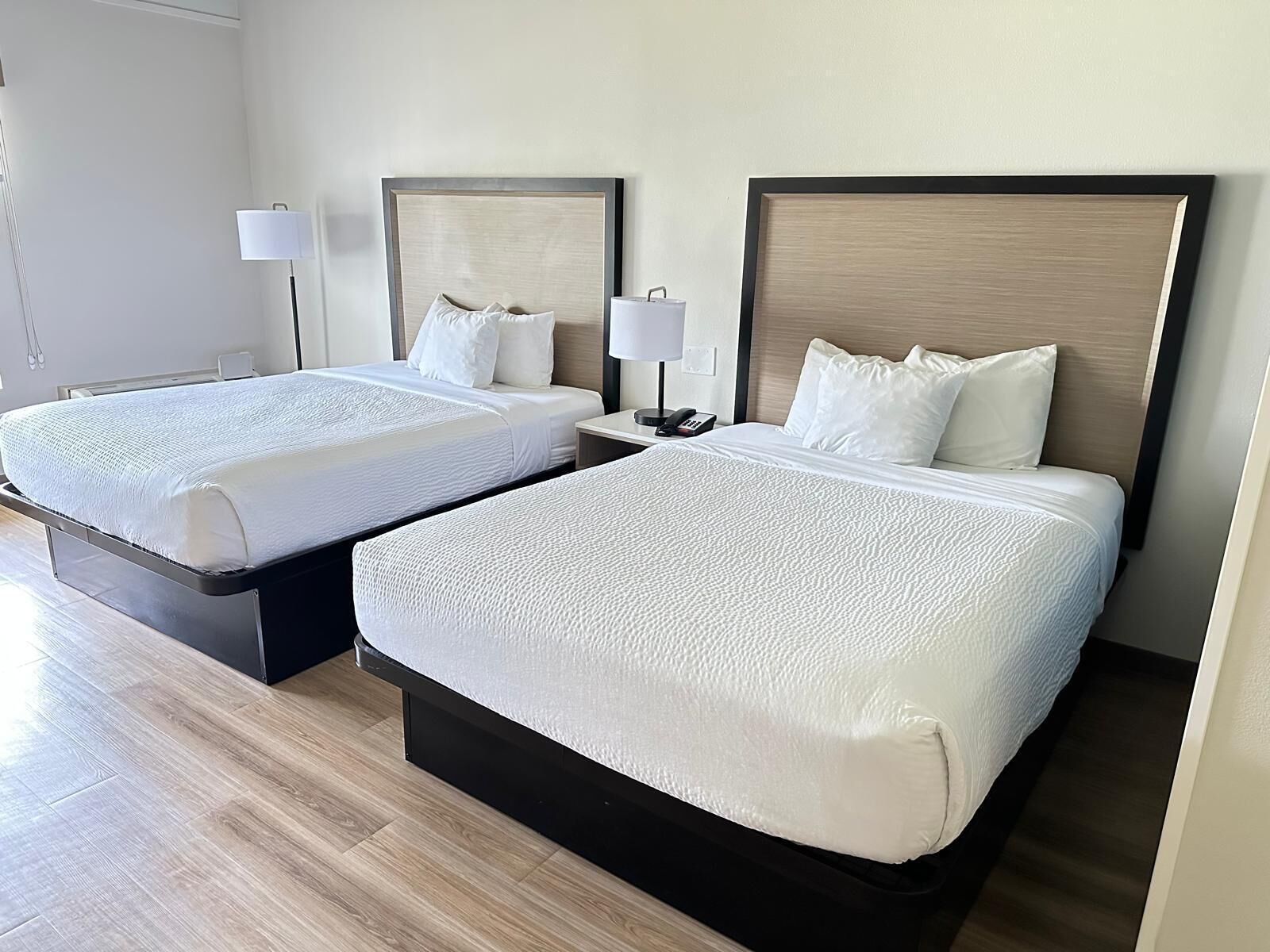 A hotel room with two beds, a bedside table with a lamp, and a phone.