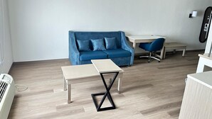 A modern living room with a blue sofa, a small table, a desk, and a chair. - Baymont By Wyndham Lexington (Lexington)