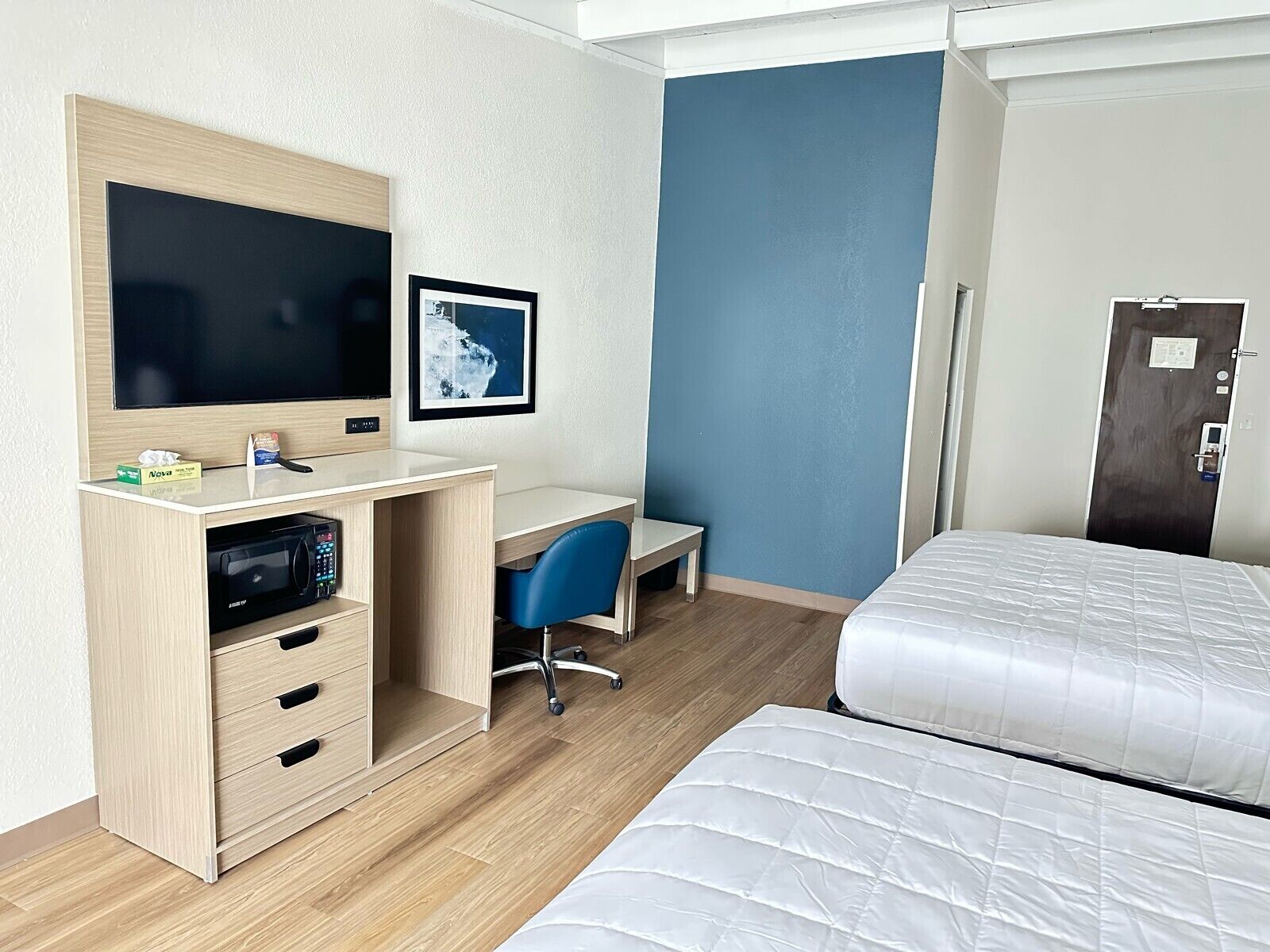 Habitació d'hotel amb un llit, escriptori amb televisió, una cadira, microones i una porta.