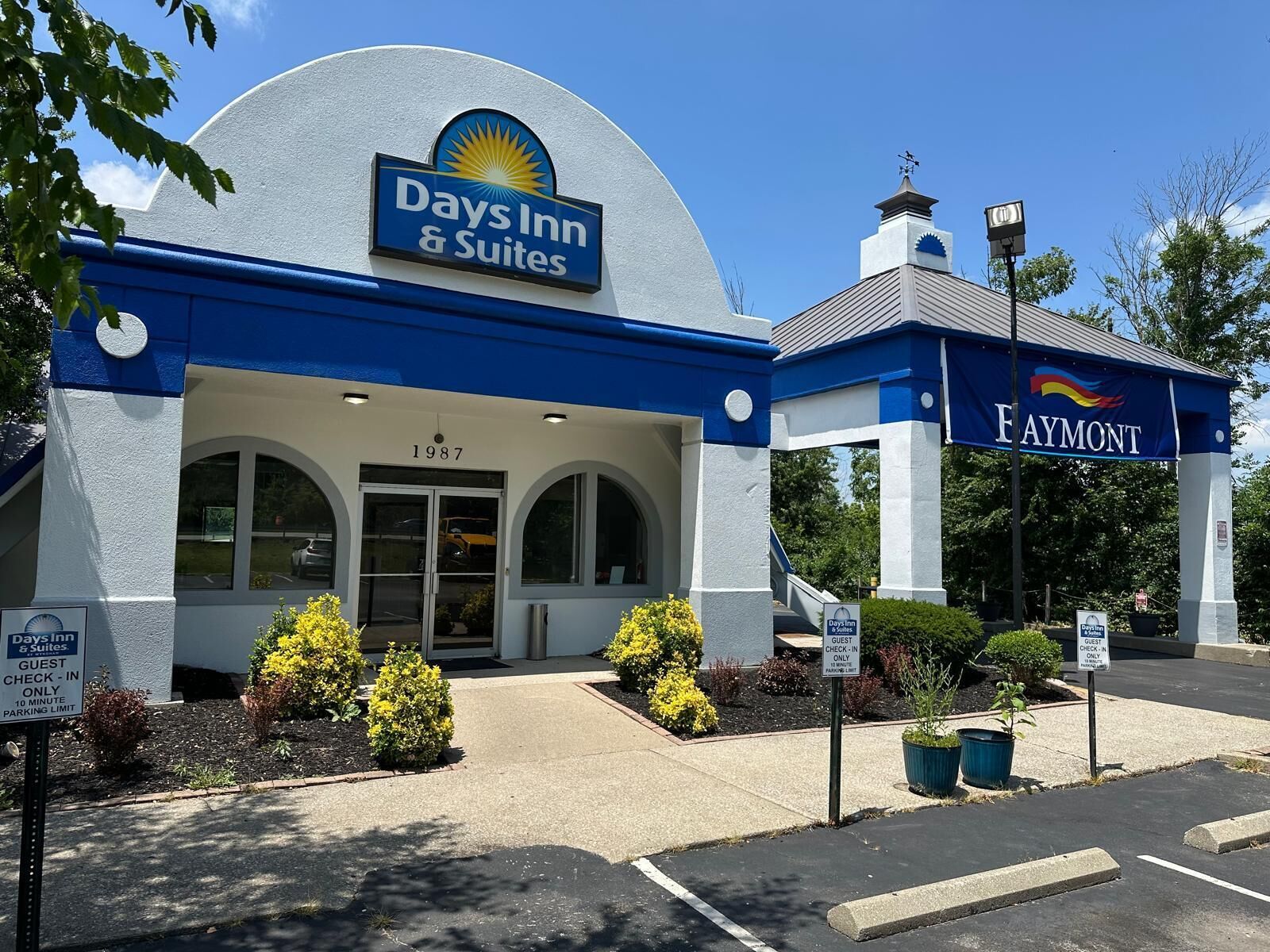 A Days Inn & Suites building with a blue and white exterior, a sign indicating guest check-in parking, and a year displayed above the entrance.