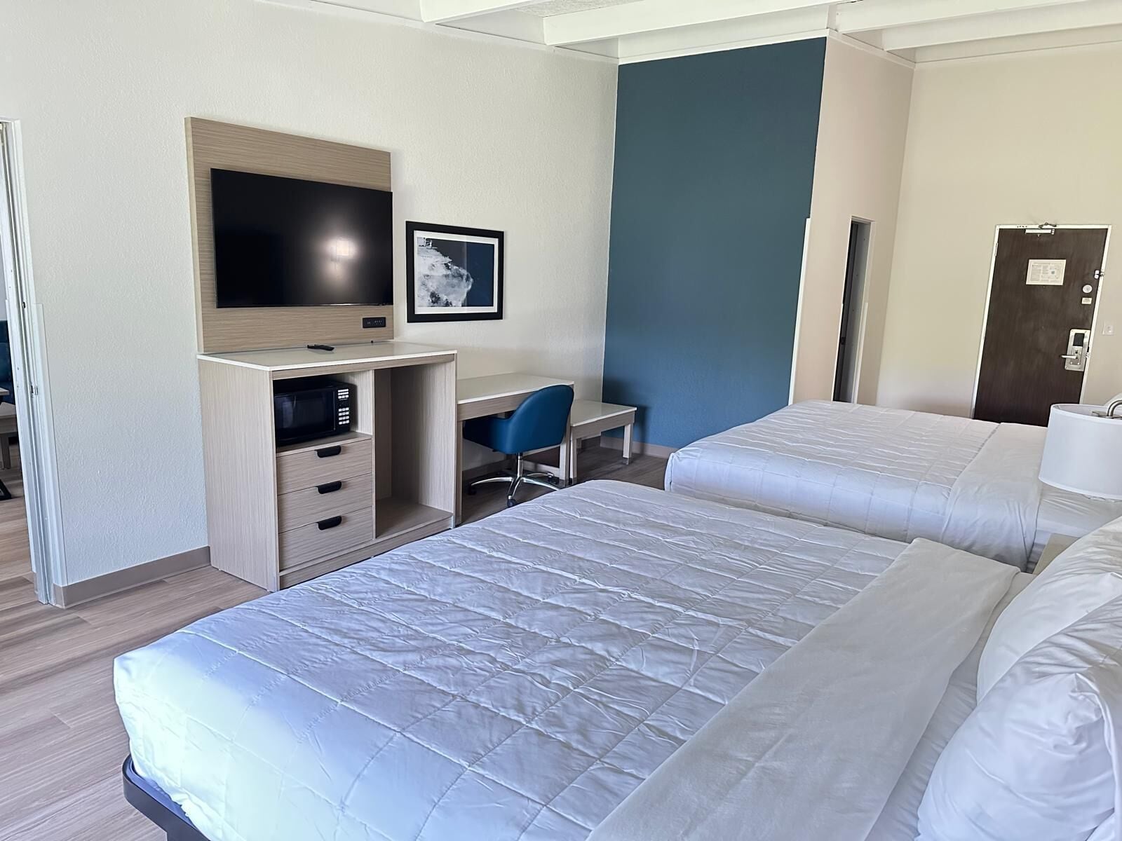 A hotel room with two beds, a desk with a chair, a television, and a picture on the wall.