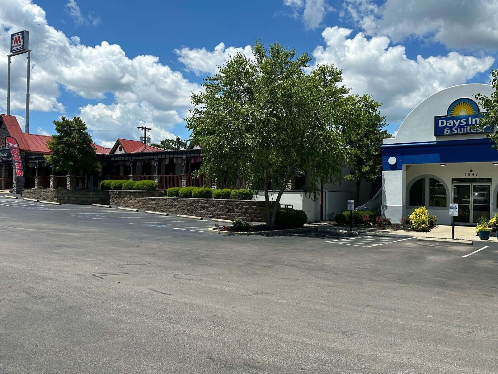 A Days Inn & Suites building with a red roof, a large tree in front, and a parking lot.