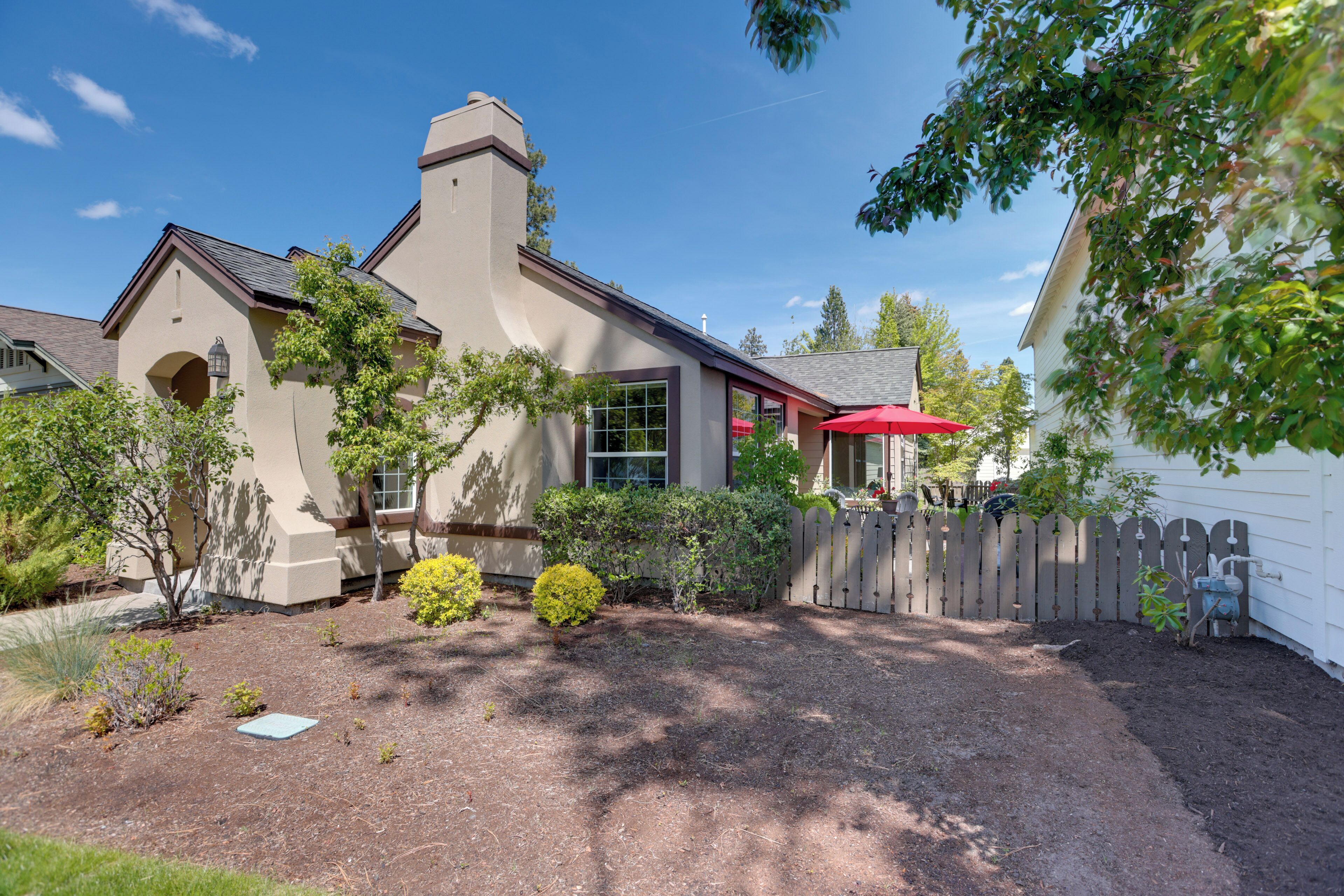 A house with a chimney, a fenced yard, and a red umbrella.