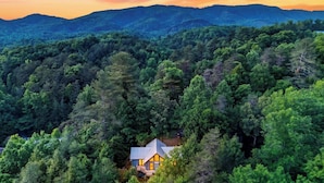 Una casa circondata da una fitta foresta, con una montagna sullo sfondo.