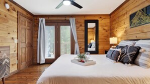 Una stanza in legno con un letto, una ventola a soffitto, una finestra con tende e uno specchio appeso al muro.