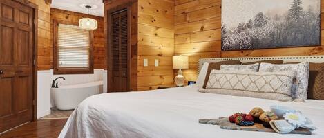 A wooden cabin-style bedroom with a large bed, a built-in bathtub, and a wall-mounted artwork.