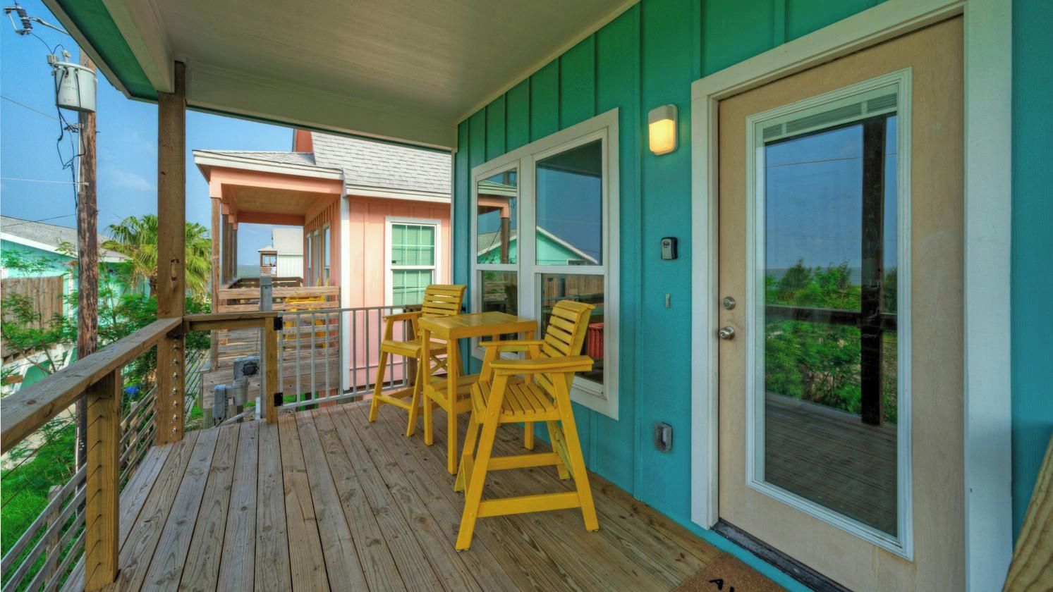 A wooden deck with outdoor seating, a sliding glass door, and a view of a neighboring building.