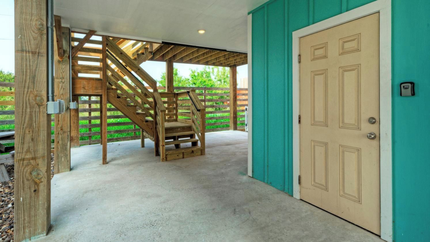 A covered outdoor area with a wooden staircase, a door, and a concrete floor.