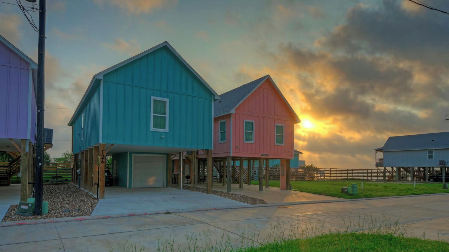 A residential area with two houses, one blue and one pink, with a garage and a driveway.