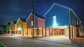 A row of colorful houses with attached garages, a clear sky, and a well-lit driveway.