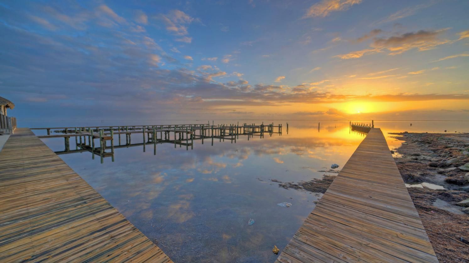 A wooden pier extending into calm waters with a sunset in the background.