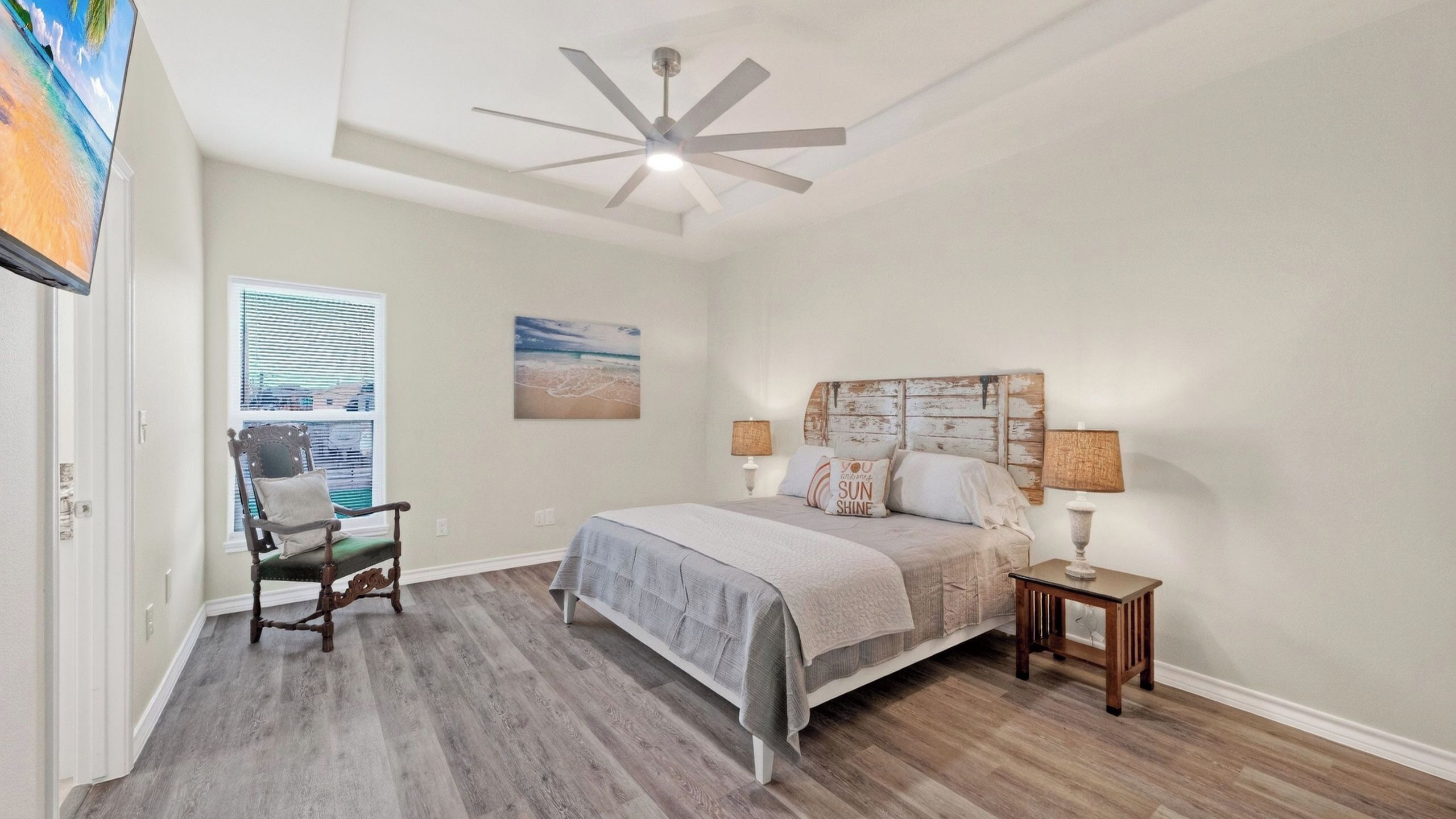 A bedroom with a bed, a chair, a nightstand, a ceiling fan, and a window with blinds.
