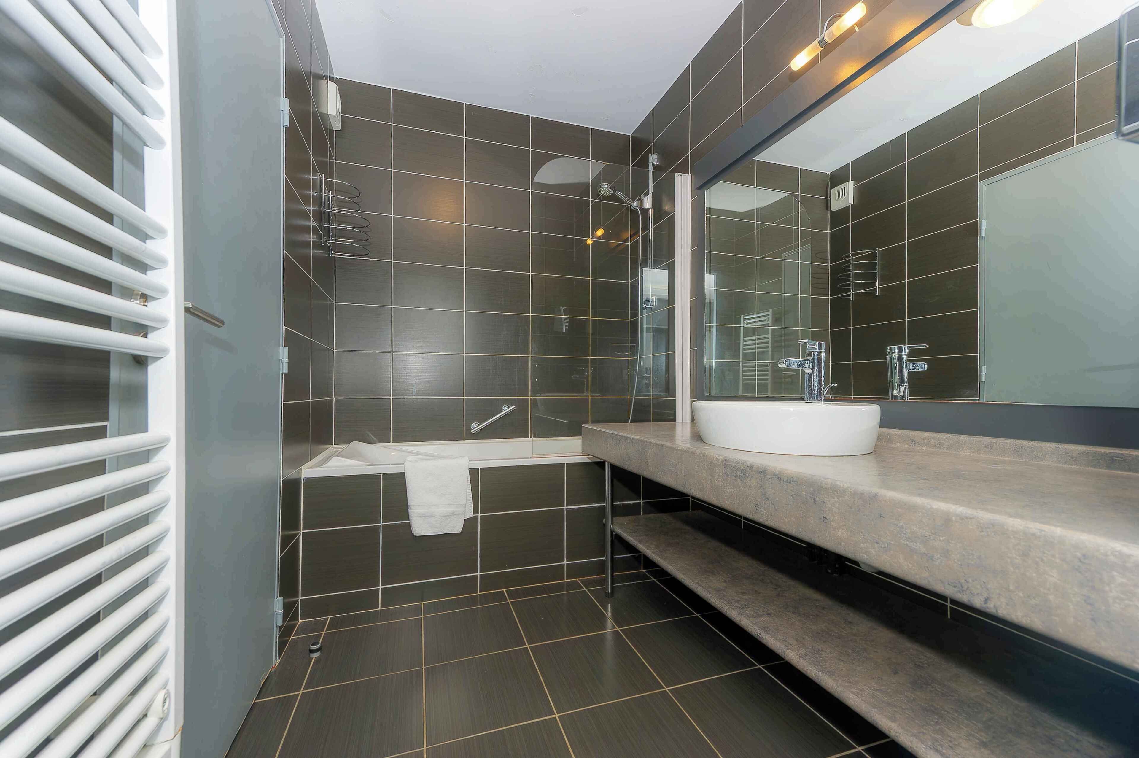 A modern bathroom with dark tiles, a white sink, and a glass shower enclosure.