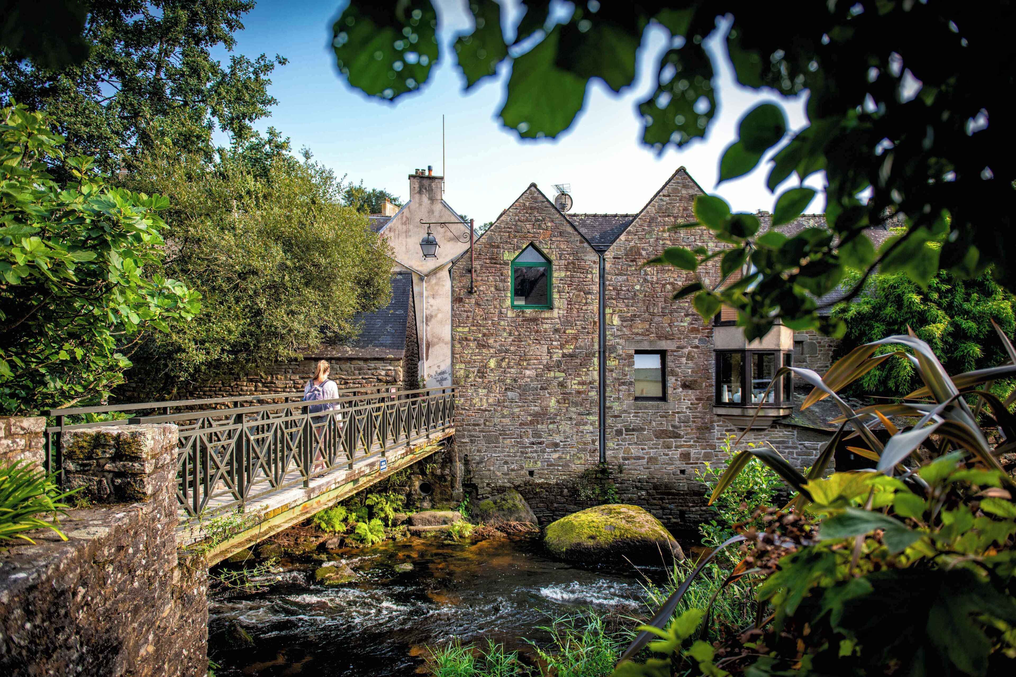Ein Steinhaus mit einer Brücke über einem Bach, umgeben von viel Grün.
