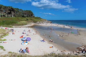 Ein Strand mit badenden Personen, Sonnenschirmen und blauem Himmel.
