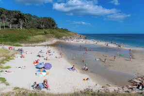 A beach with people sunbathing and swimming, surrounded by trees and the ocean.