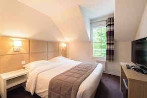 Hotellihuone, jossa on sänky, yöpöydät, televisio ja ikkuna, jossa on verhot.