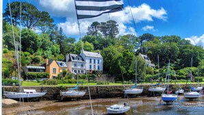 A waterfront with boats docked, a flag, and houses in the background. - Maison duplex avec wifi | Près de l'Aven (Pont-Aven)