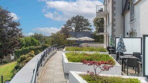 A courtyard with a pathway, outdoor seating, and a building with a balcony. - Maison duplex avec wifi | Près de l'Aven (Pont-Aven)