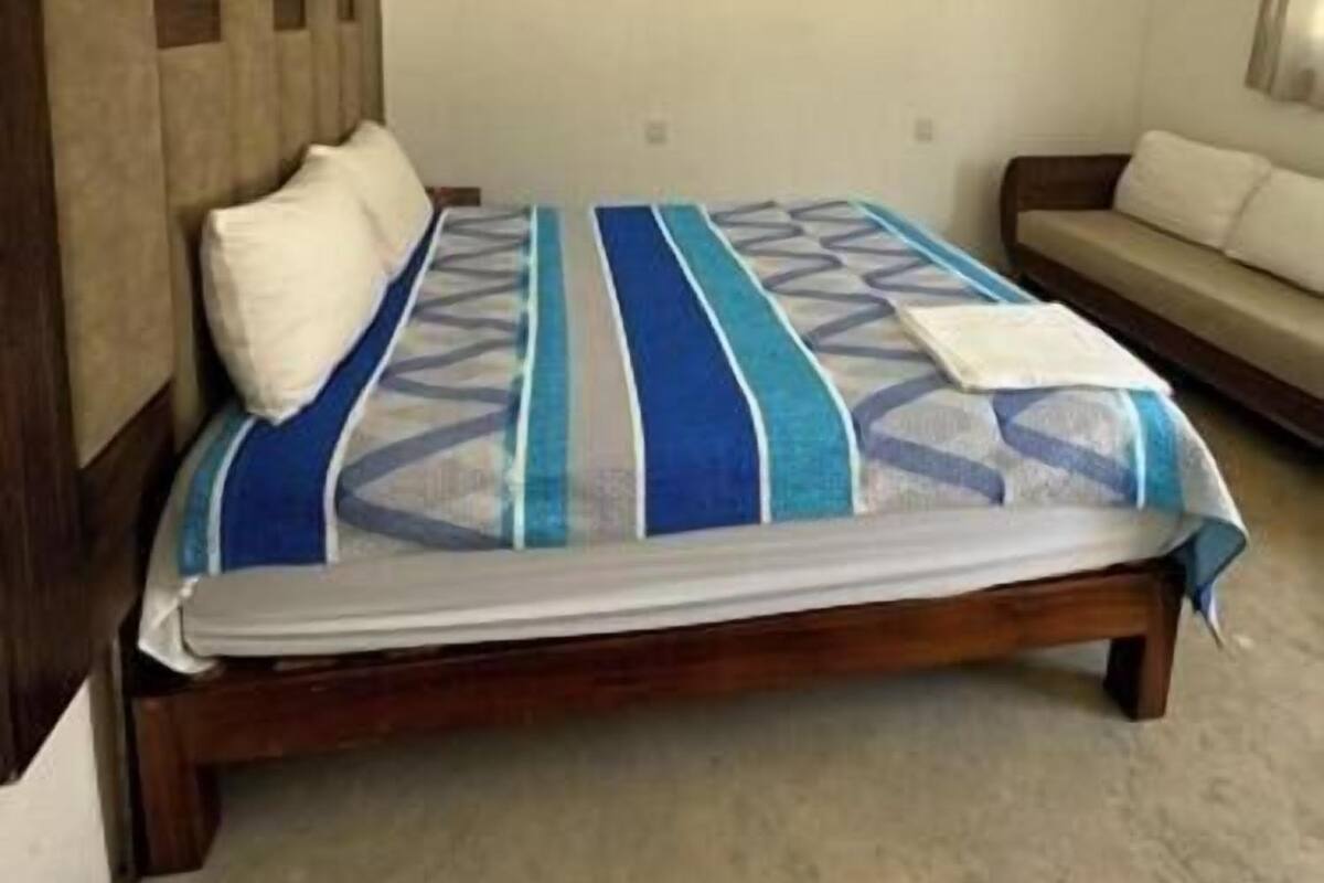 A bedroom with a bed, a ceiling fan, a sofa, and a carpeted floor.
