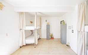 Ein Zimmer mit Etagenbetten, einem Schrank, einer Topfpflanze und einem kleinen Tisch.