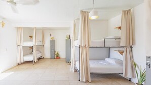 A room with bunk beds, a ceiling fan, a potted plant, and a cabinet. - Surfnest Hostel (Brisas de Zicatela)