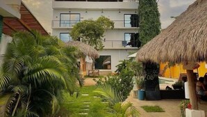 A resort with a thatched-roof building, a pool, and lush greenery. - Surfnest Hostel (Brisas de Zicatela)