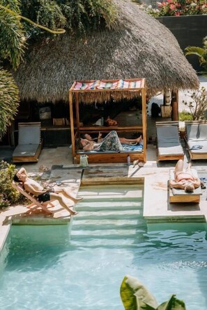 A pool area with lounge chairs, a thatched-roof structure, and a small pool. - Surfnest Hostel (Brisas de Zicatela)