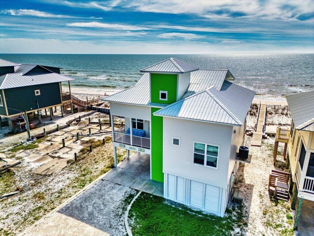 A coastal property with a two-story house, a green accent wall, and a view of the ocean.