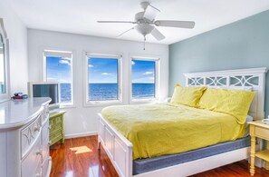 Un dormitorio con cama, ventilador de techo, cómoda y vista al océano.